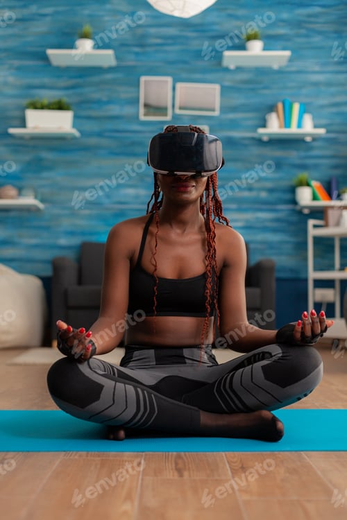 Preview: Calm tranquil black woman wearing vritual reality goggles sitting on yoga mat