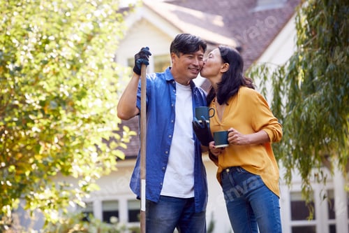 Preview: Loving Mature Asian Couple Taking A Break With Hot Drinks Whilst Tidying Garden With Rake