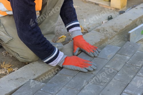 Preview: Professional worker layers installing laying gray concrete brick the street in city
