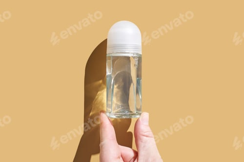 Preview: Hand holding transparent roll-on deodorant bottle against light brown