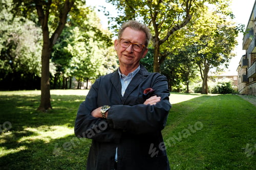 Preview: Senior man smiling with crossed arms in city park