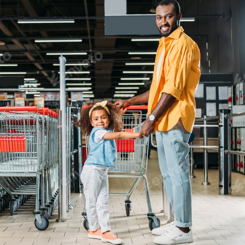 Preview: smiling african american man standing with daughter near shopping trolley in supermarket