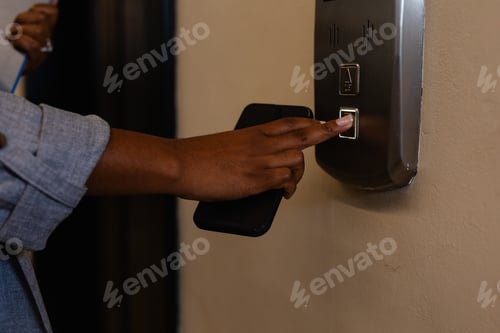 Preview: Hand of plus size african american casual businesswoman pressing elevator button in office corridor