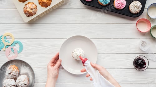 Preview: Cropped view of woman decorating cupcake with icing bag on table with cupcake trays
