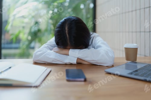 Preview: A young woman sits at her desk, head resting on her arms, expressing stress and fatigue in a serene