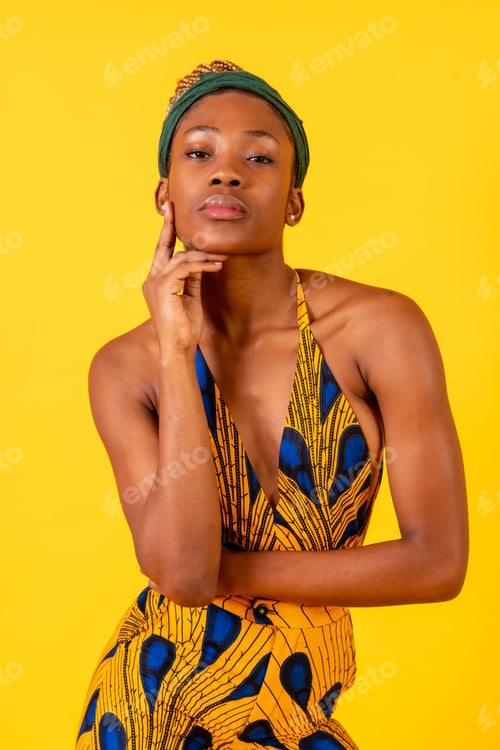 Preview: African young woman in the studio on a yellow background, portrait in a traditional costume looking