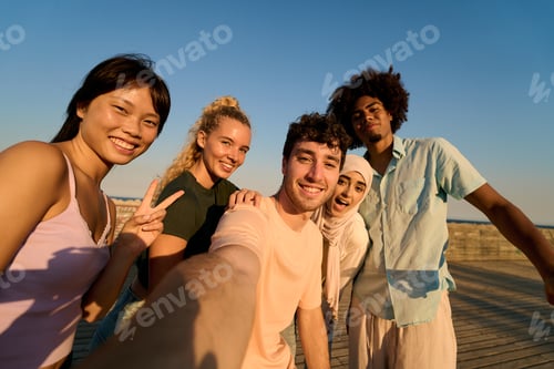 Preview: Happy multi ethnic friends taking selfie on pier at sunset