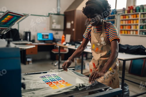 Preview: Smiling diverse graphic worker putting screen printed t-shirt into dryer