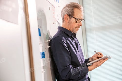 Preview: Male digital designer leaning against office wall making notes