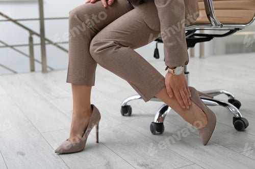 Preview: Young woman suffering from leg pain in office, closeup