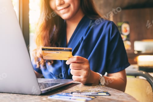 Preview: Closeup image of a business woman holding credit card while using laptop computer