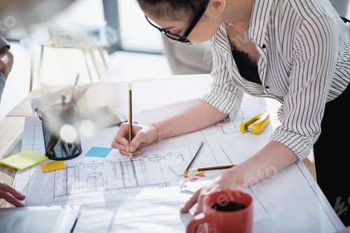 Preview: Young asian businesswoman in eyeglasses working with blueprint in office