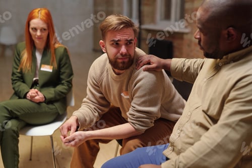 Preview: Young bearded man crying while looking at African guy supporting him