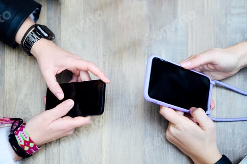 Preview: Female hands with mobile phones on the table from above