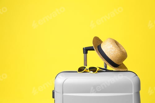 Preview: Stylish grey suitcase with hat and sunglasses on yellow background. Space for text