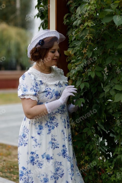 Preview: A woman in vintage clothes and a hat stands against the background of a fountain in an autumn park