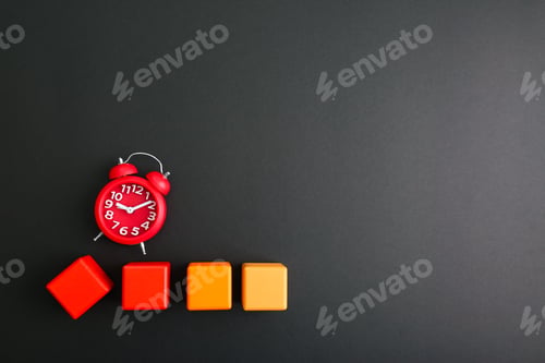 Preview: Alarm clock and colorful wooden cubes on black background, flat lay. Space for text