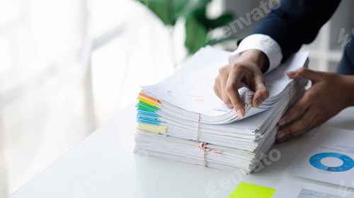 Preview: Businessman looking through stacks of papers on desk, corporate financial papers.