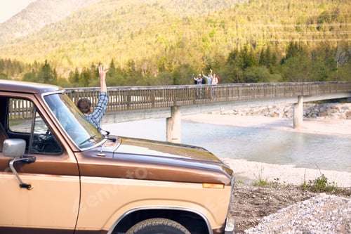 Preview: Man standing by vehicle waving at people on bridge in the background