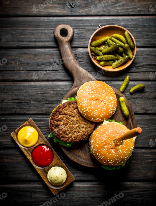 Preview: Burgers on a cutting Board with a knife and gherkins in a bowl.