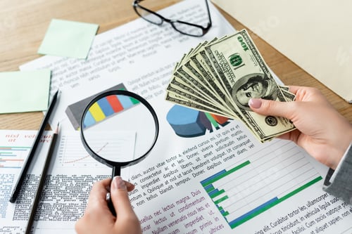 Preview: top view of tax inspector holding magnifier and glasses above charts and dollar banknotes