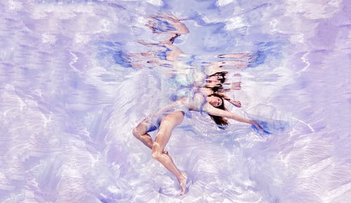 Preview: Underwater view of woman draped in sheer fabric, floating towards water surface