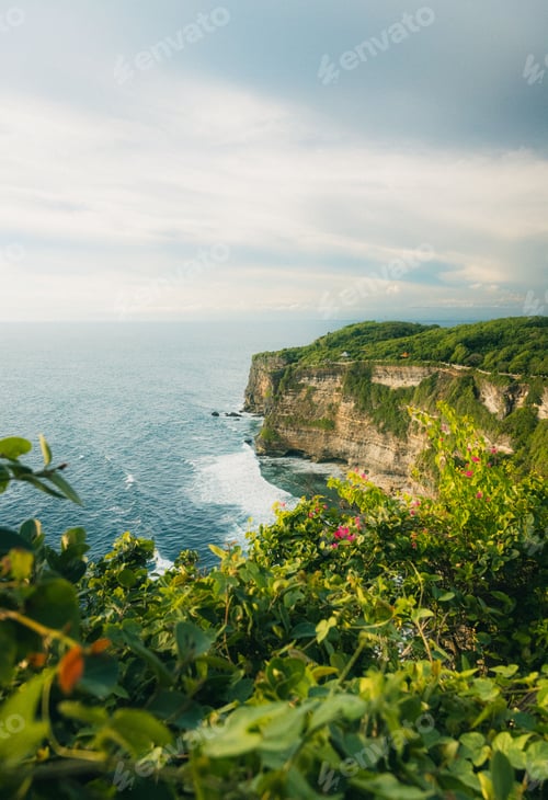 Preview: Scenic view of Uluwatu Cliff in Bali with lush greenery and the ocean under a partly cloudy sky