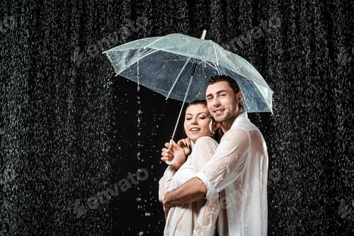 Preview: side view of romantic couple in white shirts standing under umbrella under raindrops isolated on