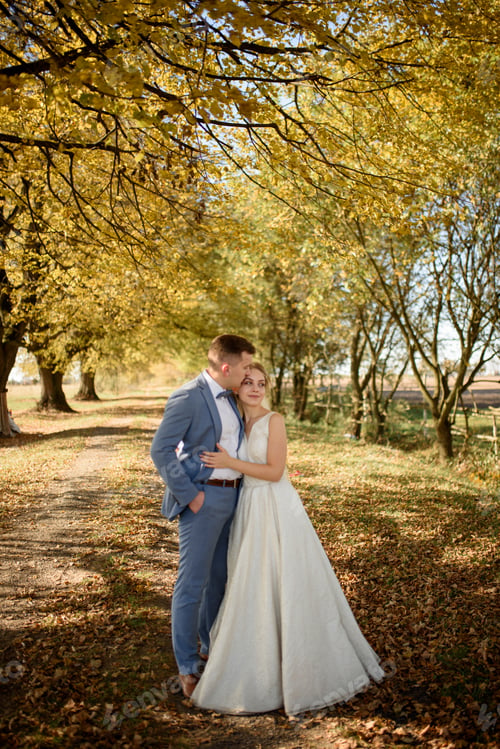 Preview: Young beautiful couple hugging in their wedding dresses in autumn park.