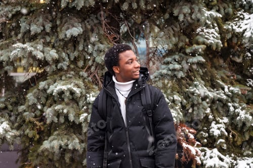 Preview: African american man posing in snowy winter at fir tree background, looking away