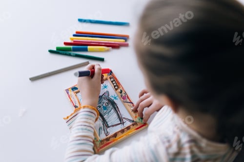 Preview: A girl sits at a table and draws, decorates a frame for a photo with drawing, children creativity