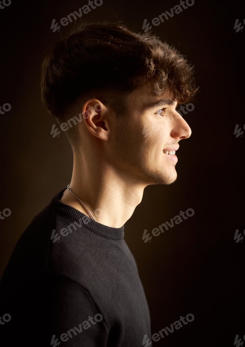 Preview: Young man smiling and looking right on dark background
