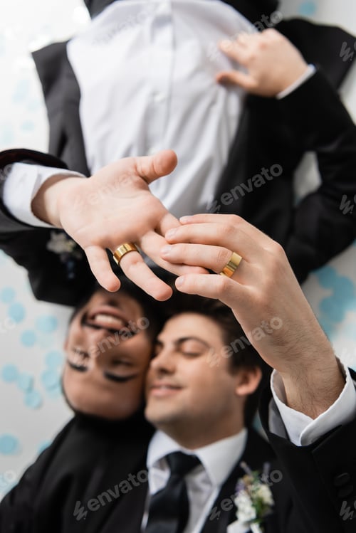 Preview: Top view of blurred same sex grooms in suits touching fingers of each other in wedding rings