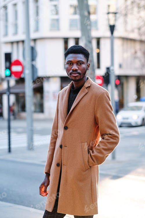 Preview: Stylish African American man looking at camera while posing outdoors on the street.