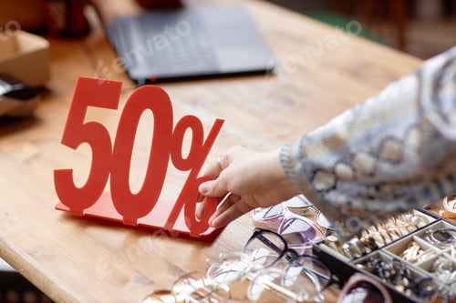 Preview: Hand Placing Fifty Percent Discount Sign on Table at Thrift Store