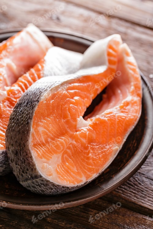 Preview: Cooking two fresh raw salmon fish steaks on wooden rustic table closeup