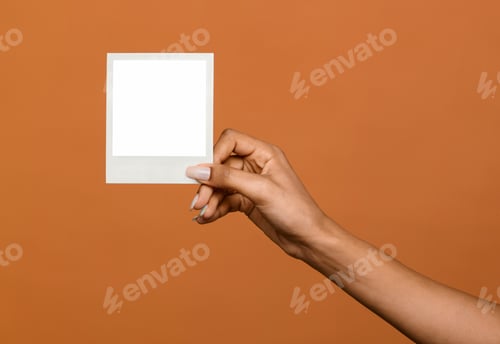 Preview: Black female hand holding up a blank instant photo frame