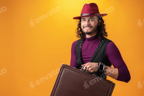 Preview: Young man with cirly long hair showing a briefcase against yellow background