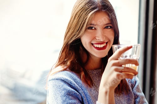Preview: Happy stylish woman holding glass of drink and smiling in cafe