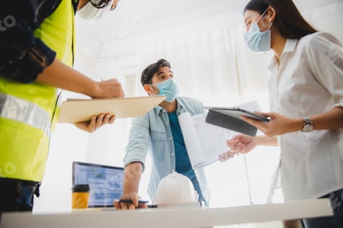 Preview: Hand of engineer point to blue print with team wearing mask work and planning in office
