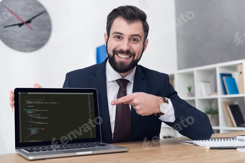Preview: portrait of smiling businessman pointing at laptop at table in office