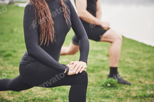 Preview: Fitness couple stretching outdoors in park near the water. Young bearded man and woman exercising