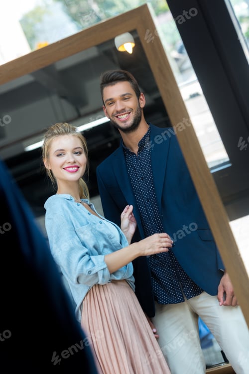 Preview: beautiful smiling young couple looking at mirror in boutique