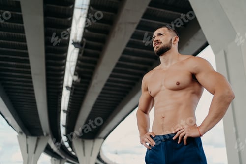 Preview: Strong man with naked torso keeps hands on waist, has muscular body after long training