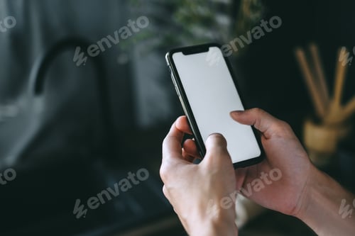 Preview: Man using a smartphone with a white blank screen in the kitchen.