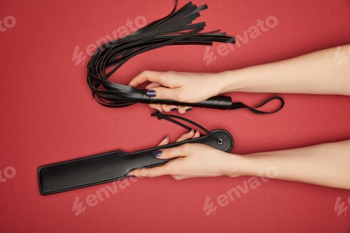 Preview: cropped view of woman with paddle and flogging whip isolated on red