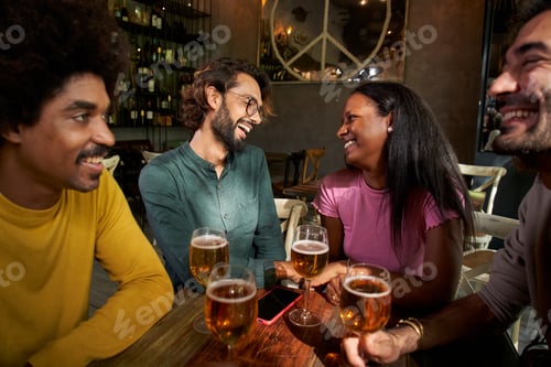 Preview: Group of young friends having beer in a bar and smiiling