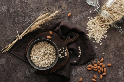 Preview: Bowl of dry oat flakes with ears of wheat and almond nuts on dark background