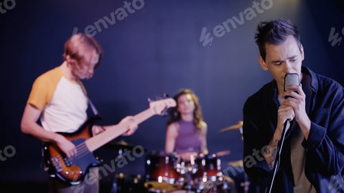 Preview: tattooed man singing on stage with blurred music band