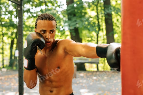 Preview: Kickboxer practicing punches at the sports ground. Young boxer working out outdoors.